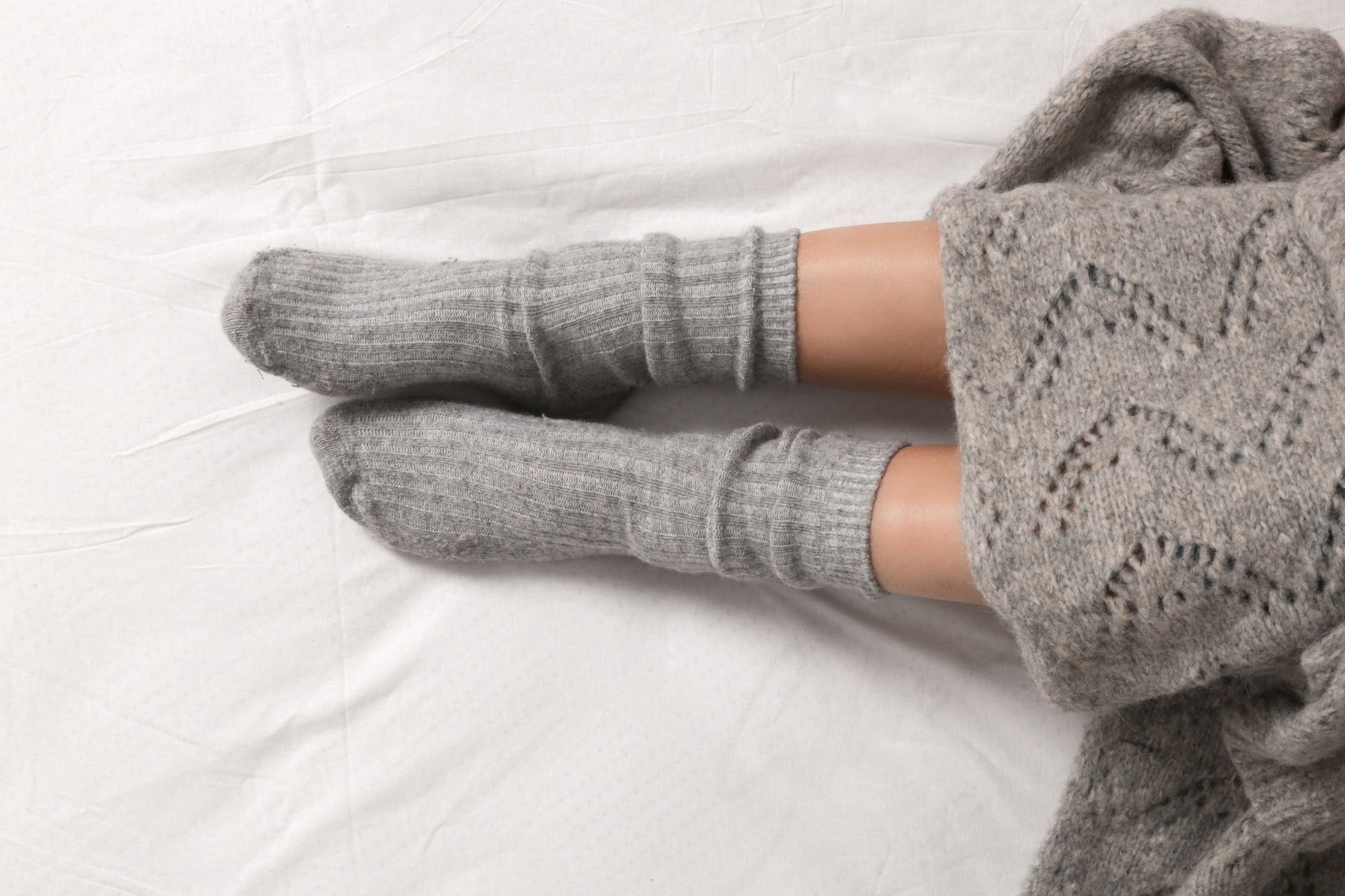 Pair of female legs wearing cozy grey cashmere socks under blanket in bed, closeup